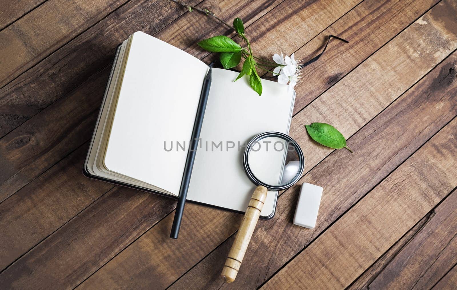 Photo of blank notebook, magnifier, pencil and eraser on wood table background.