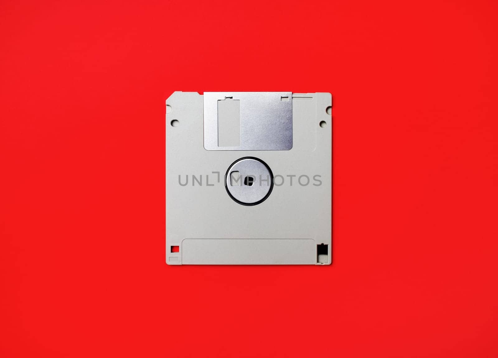 Gray diskette on red paper background. Floppy disc. Flat lay.