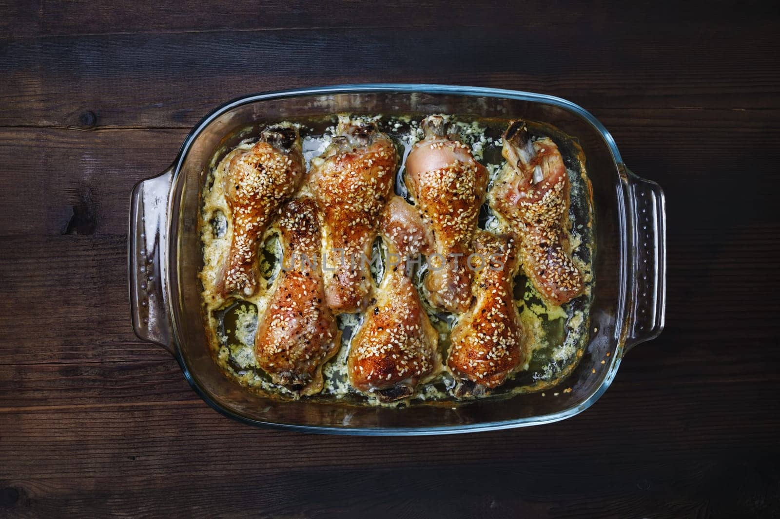 Fried chicken legs with sesame seeds in a glass tray on wooden table. Flat lay.