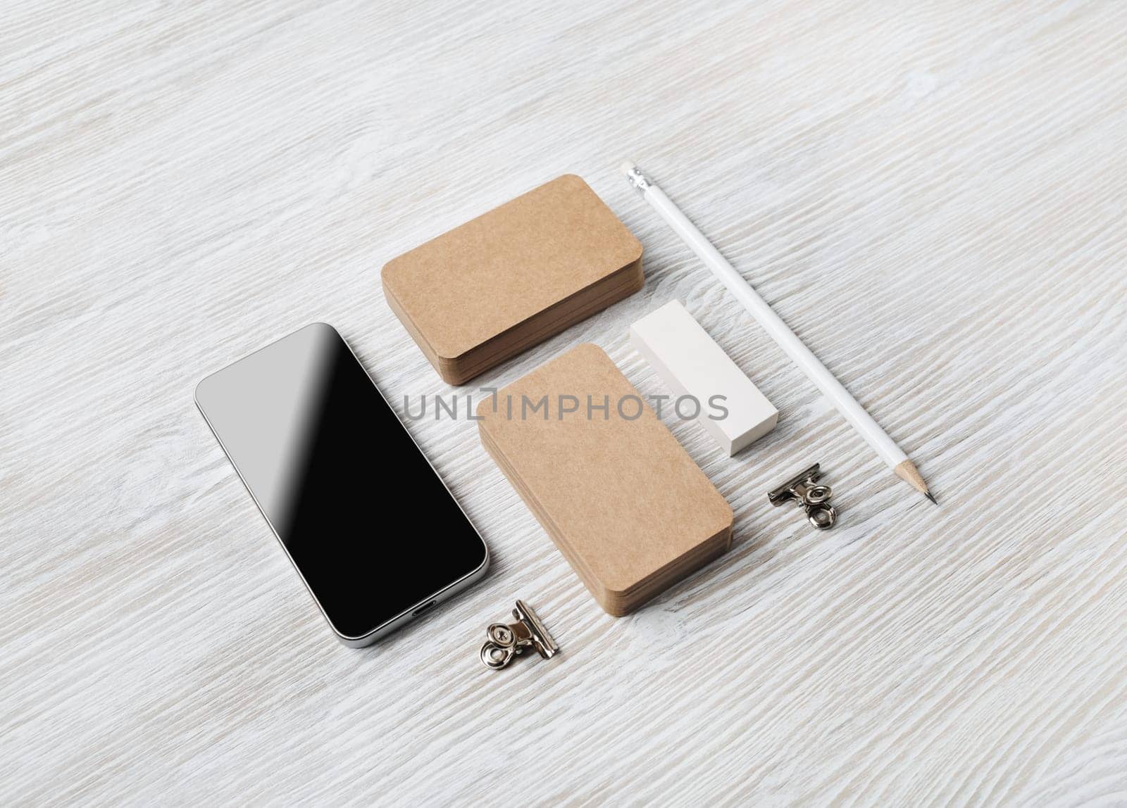 Blank stationery mockup. Blank kraft business cards, smartphone, pencil and eraser on light wooden background. Brand ID set.