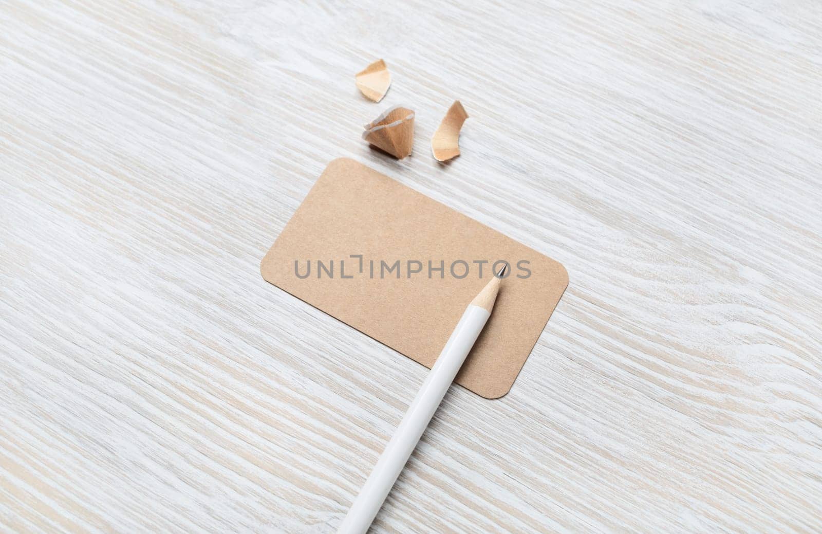 Blank kraft business card and pencil on light wood table background. Template for graphic designers portfolios.