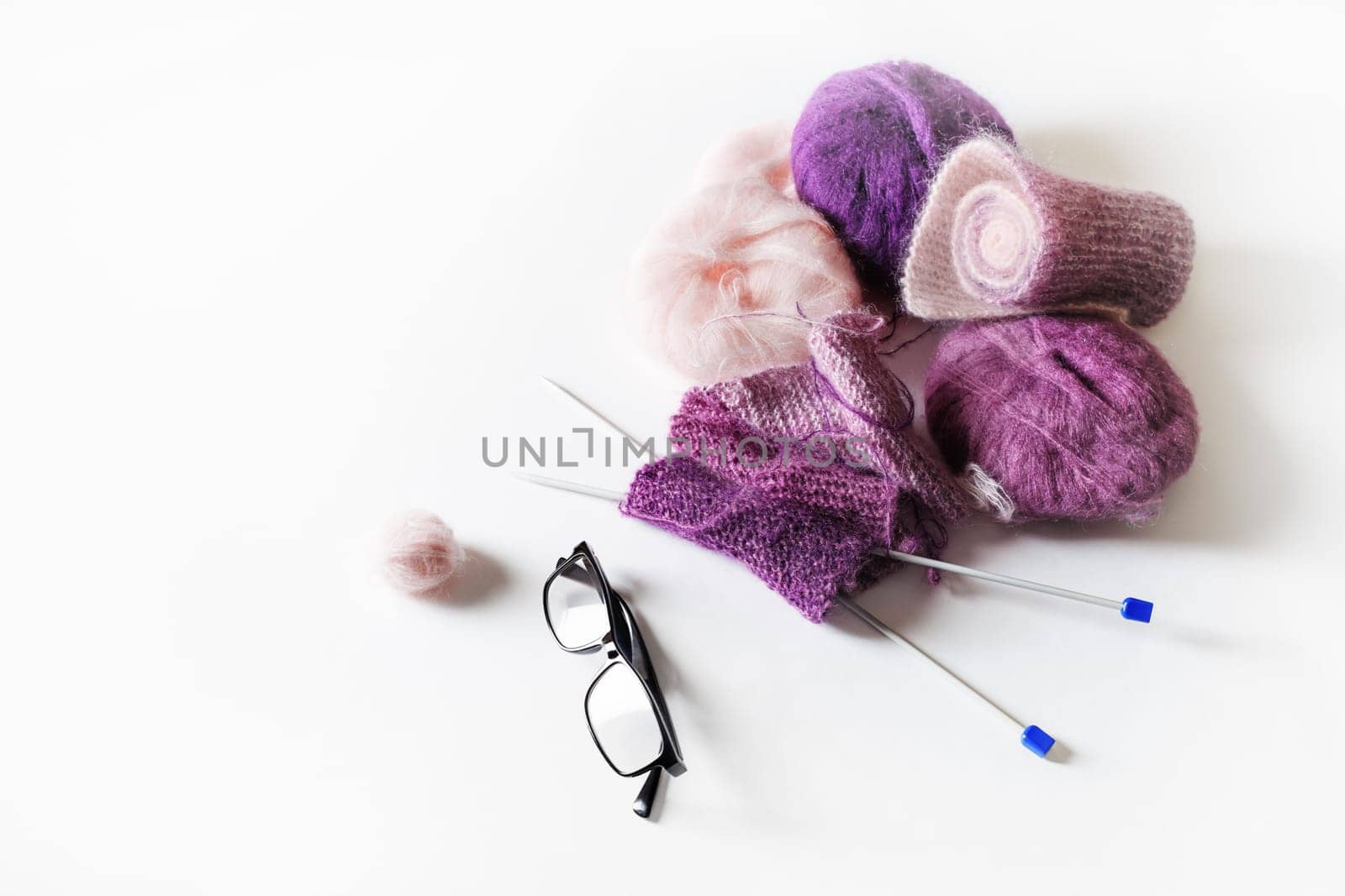 Knitting threads, knitting needles and glasses on white table background.