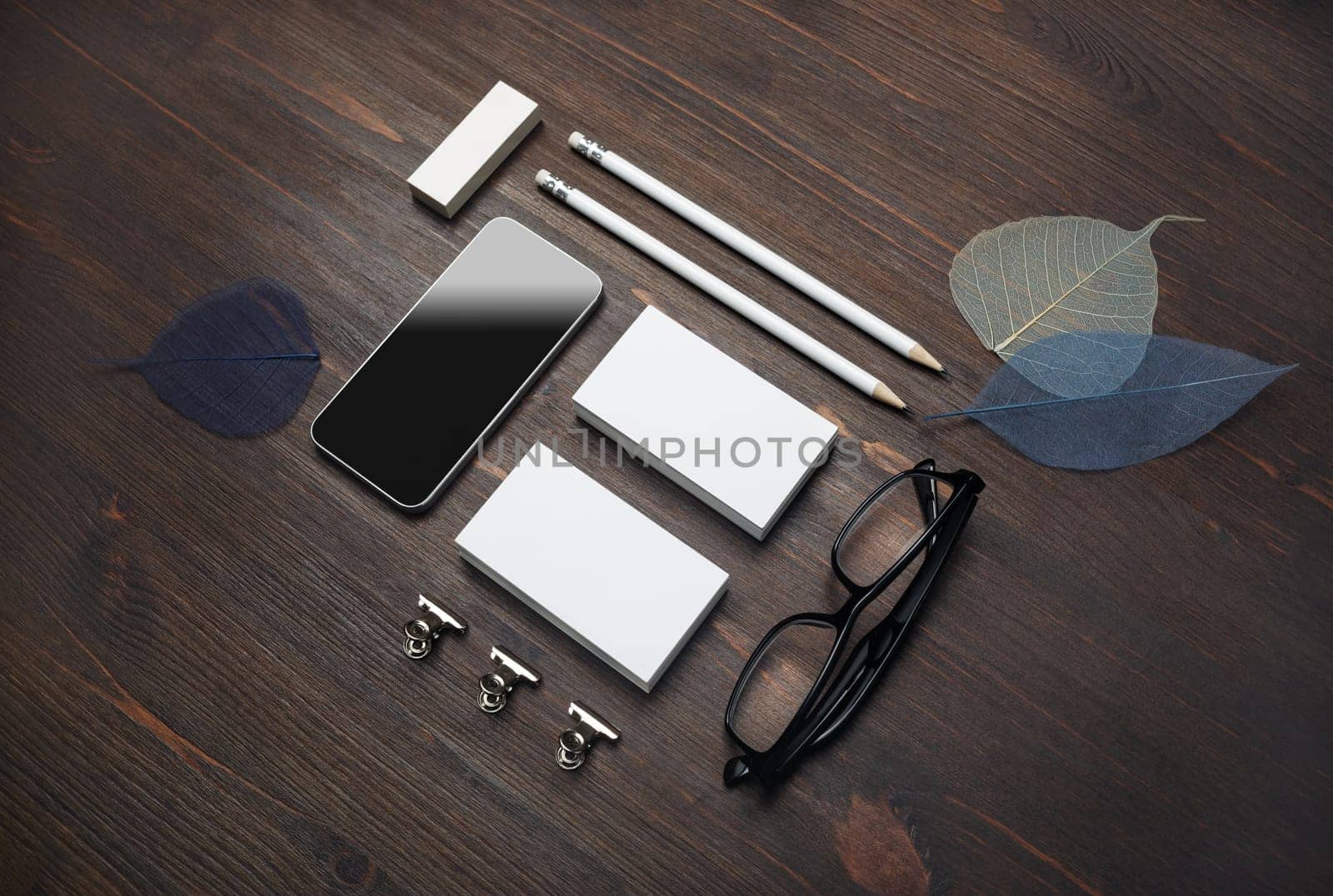 Branding stationery template. Blank business cards, smartphone, pencils, eraser, glasses and leaves on wood table background. For design presentations and portfolios.