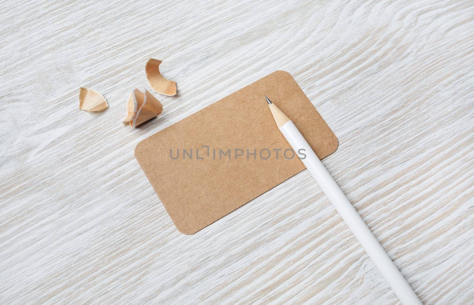 Blank kraft business card and pencil on light wooden background. Mock-up for branding identity.