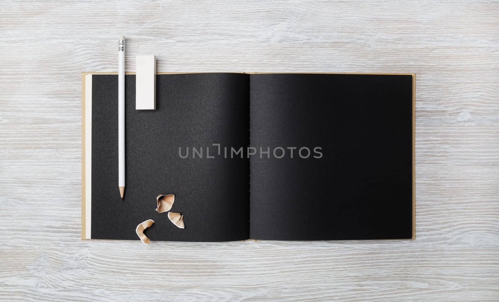 Blank black booklet, pencil and eraser on light wooden background. Branding mock up. Flat lay.