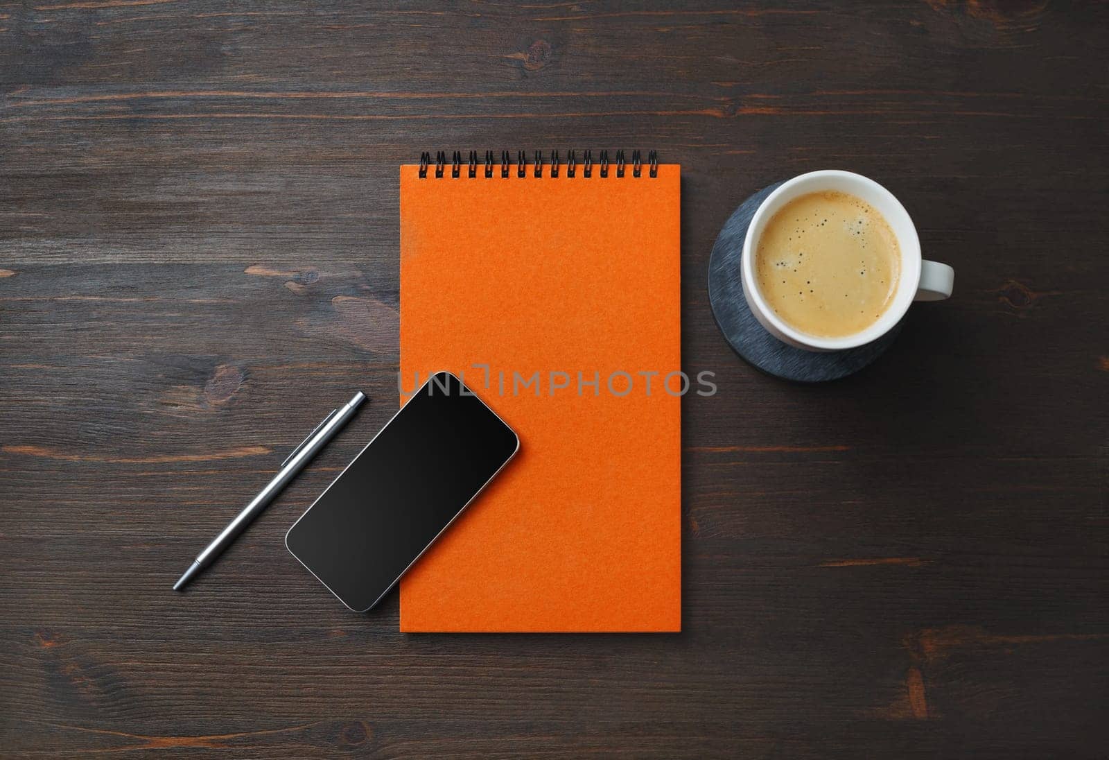 Orange notebook, smartphone, coffee cup and pen on wood table background. Blank branding template. Flat lay.