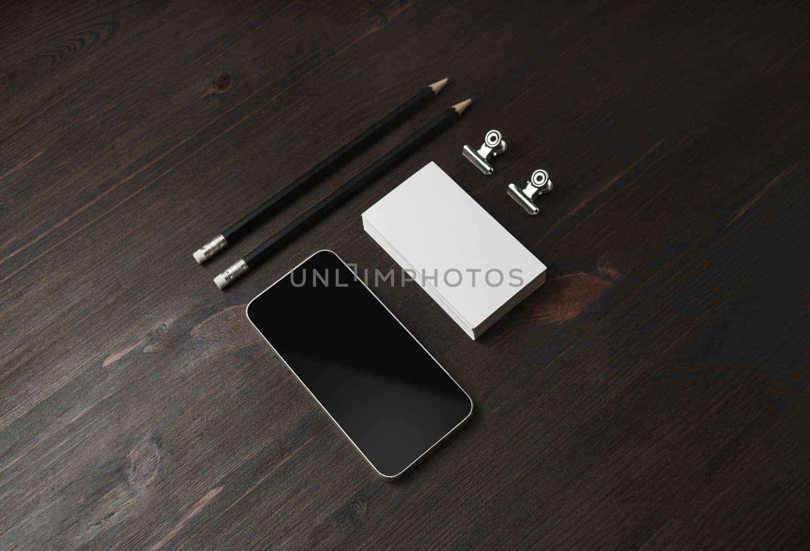 Blank stationery template on wooden background. Smartphone, business cards, pencils and paper clips.