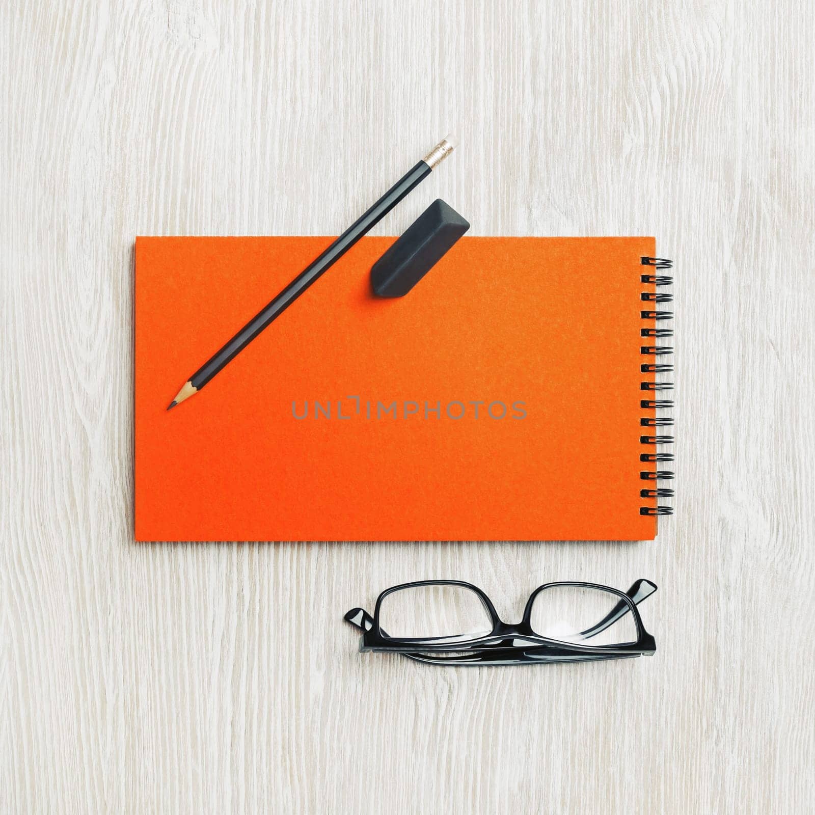 Blank orange sketchbook, glasses, pencil and eraser on light wood table background. Template for branding design. Flat lay.
