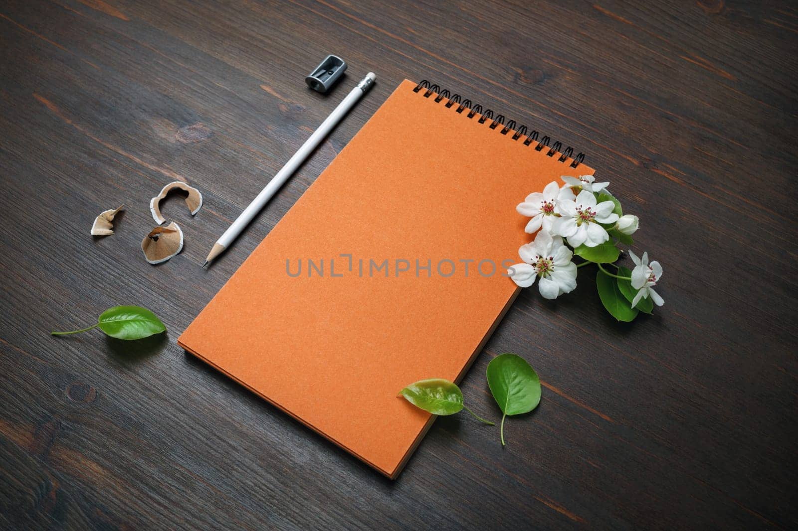 Blank stationery set on wooden background. Orange notebook, pencil, sharpener and flowers.