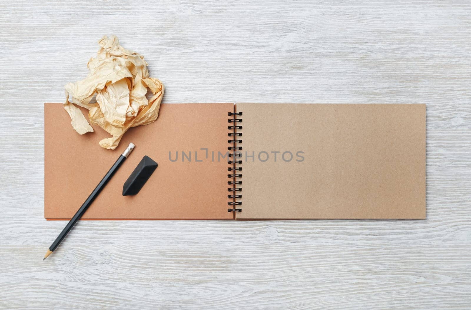 Photo of open blank kraft notebook, pencil, eraser and crumpled paper on light wood table background. Responsive design template. Flat lay.