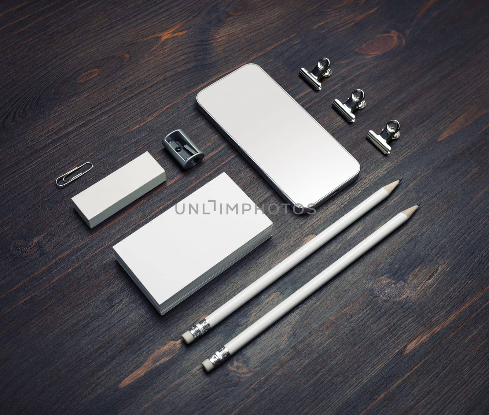 Photo of blank smartphone, business cards, pencils, eraser and sharpener on wood table background. Stationery mock up.