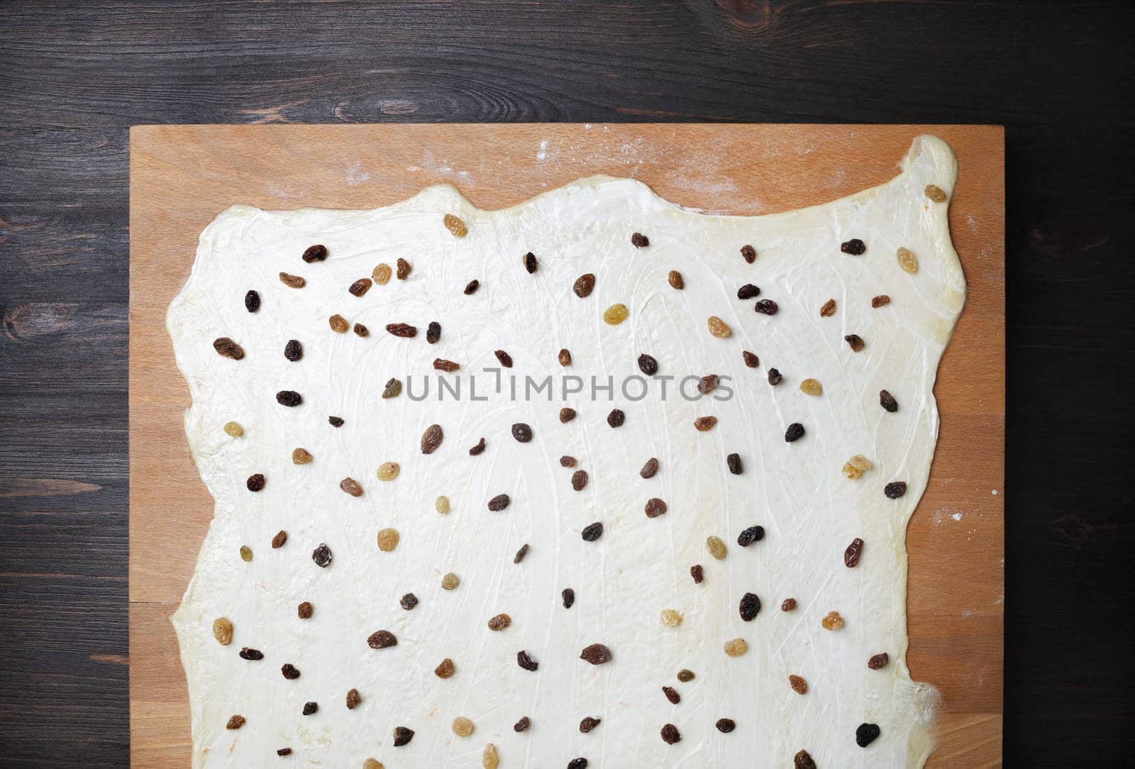 Rolled dough with raisins on wooden cutting board. Top view. Flat lay.