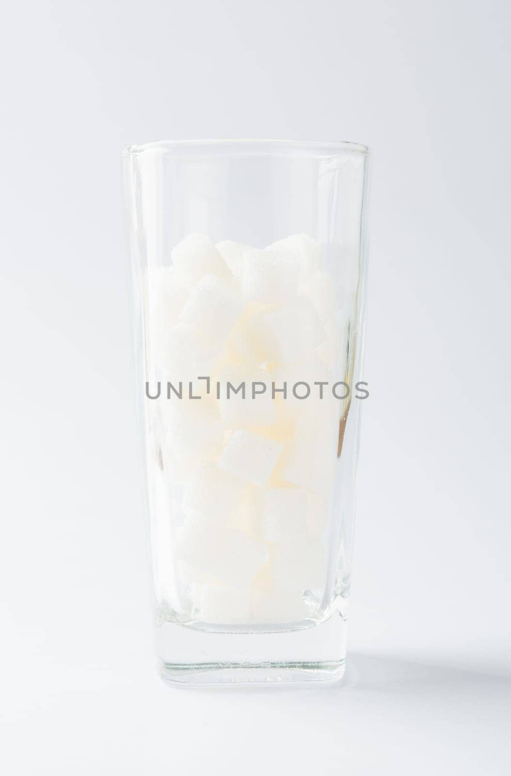 A glass full of white sugar cube sweet food ingredient, studio shot isolated on white background, health high blood risk of diabetes and calorie intake concept and unhealthy drink