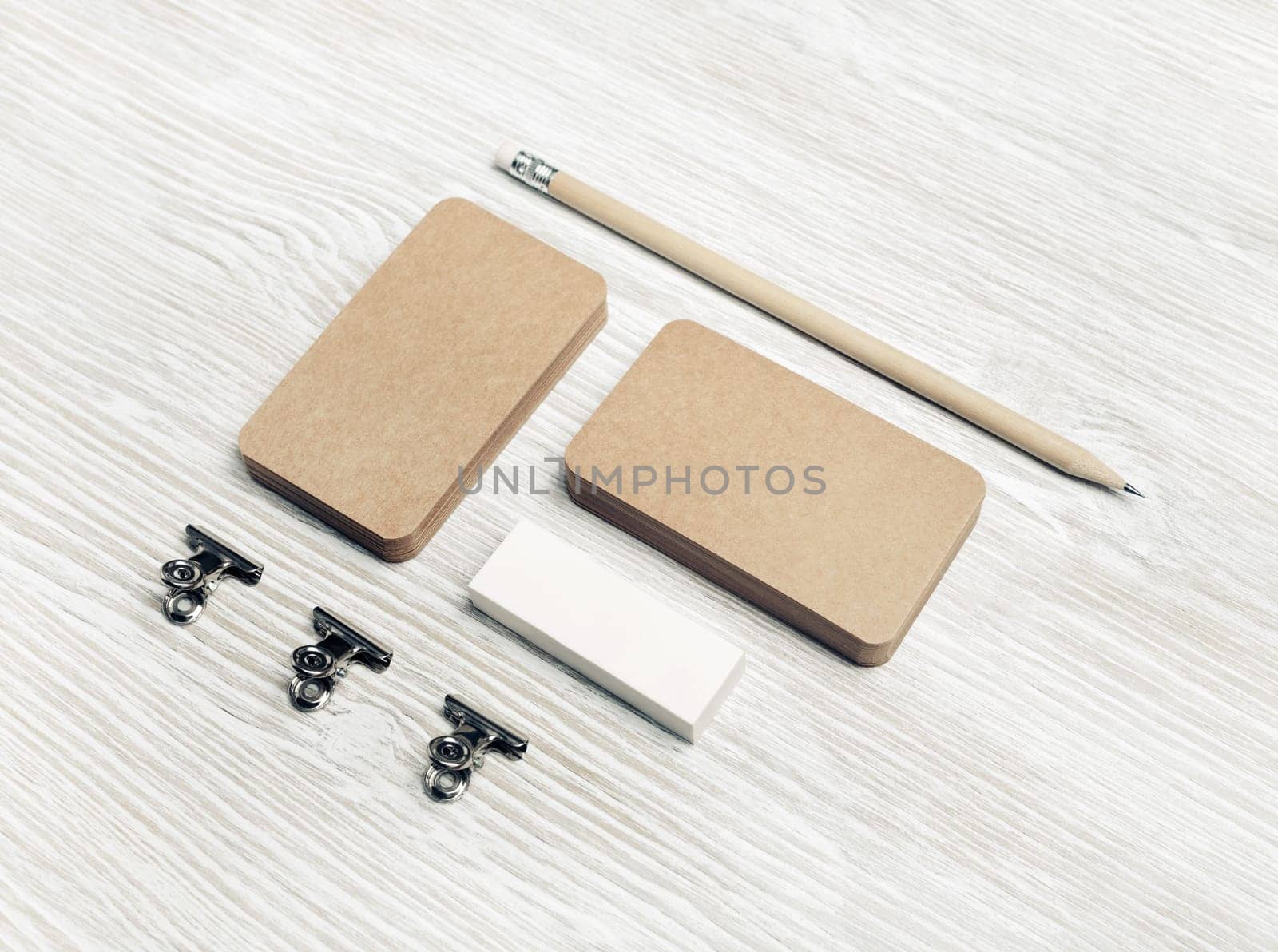 Blank kraft business cards, pencil and eraser on light wood table background. Branding mock up.