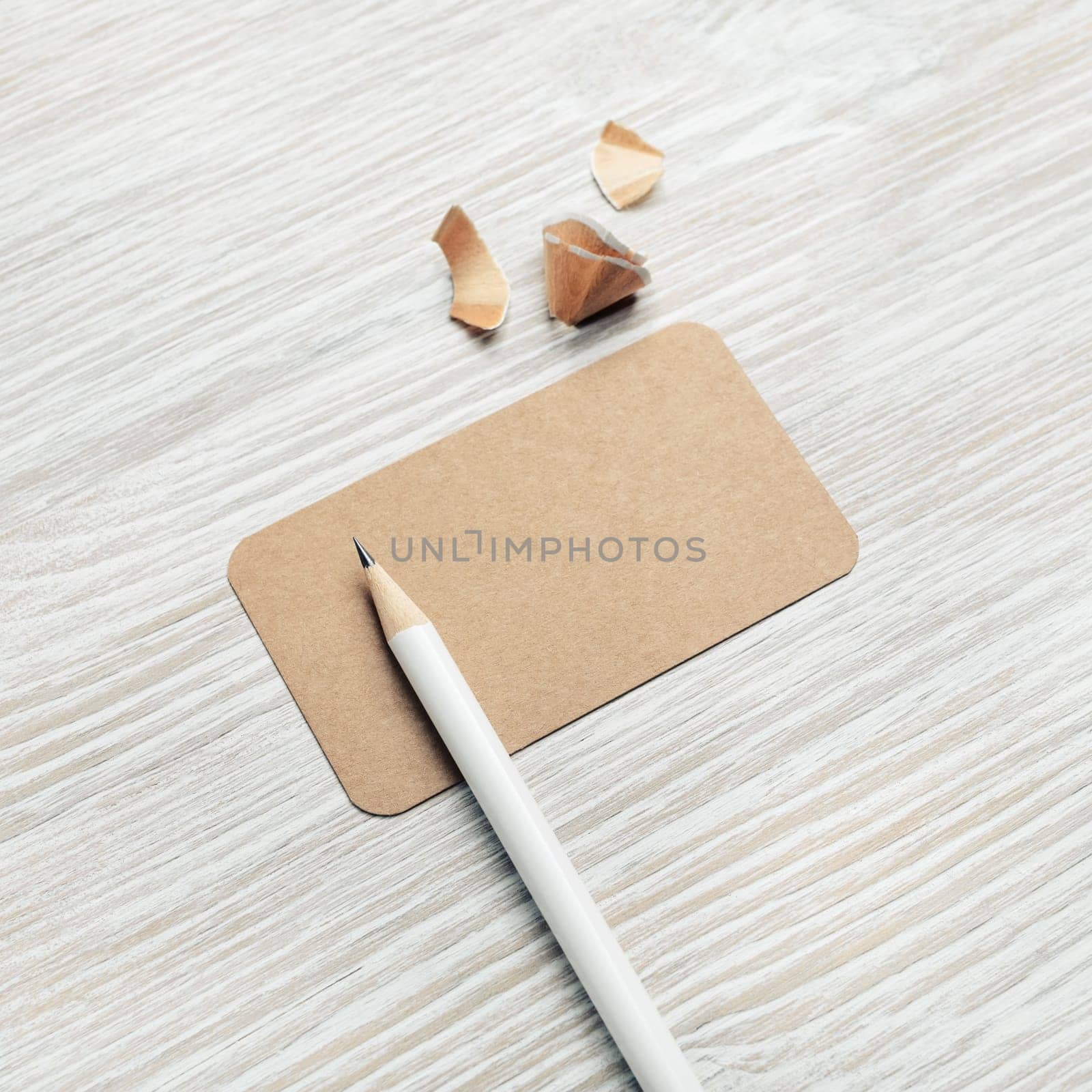 Photo of blank vintage business card and pencil on light wooden background. Mockup for ID.