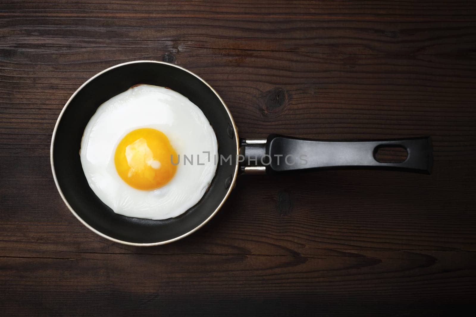 Fried egg in frying pan on wooden background. Flat lay.