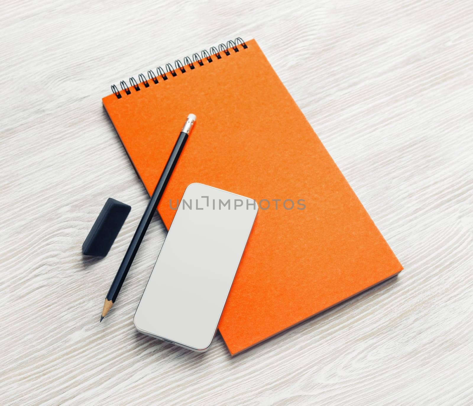 Blank orange notebook, smartphone, pencil and eraser on light wooden background. Stationery mock up.
