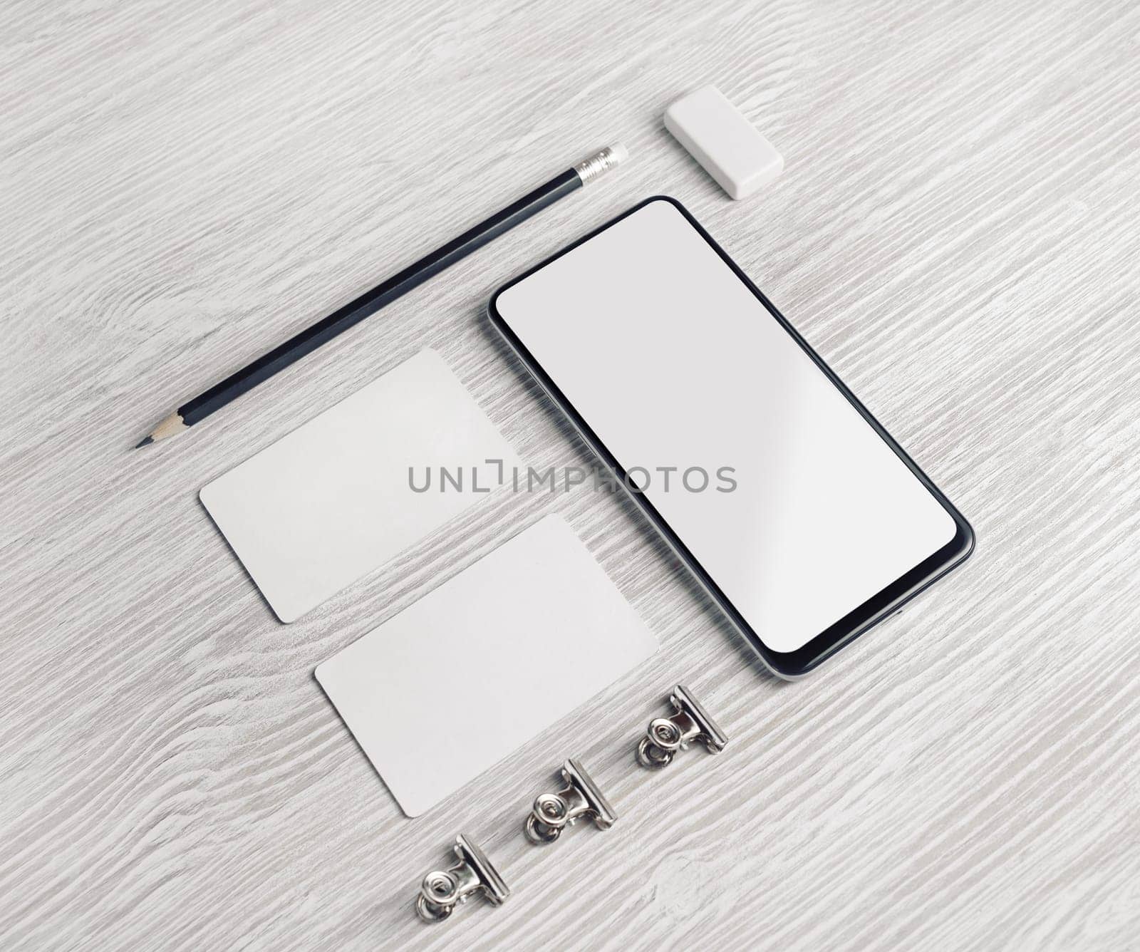 Smartphone, blank business cards, pencil and eraser on light wood table background. Branding identity mock up.