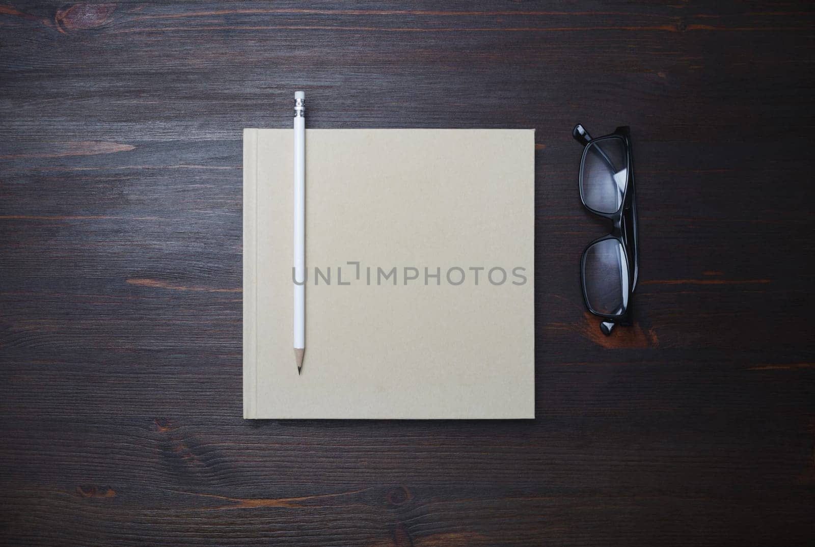 Blank closed book, pencil and glasses on wood table background. Stationery template. Flat lay.