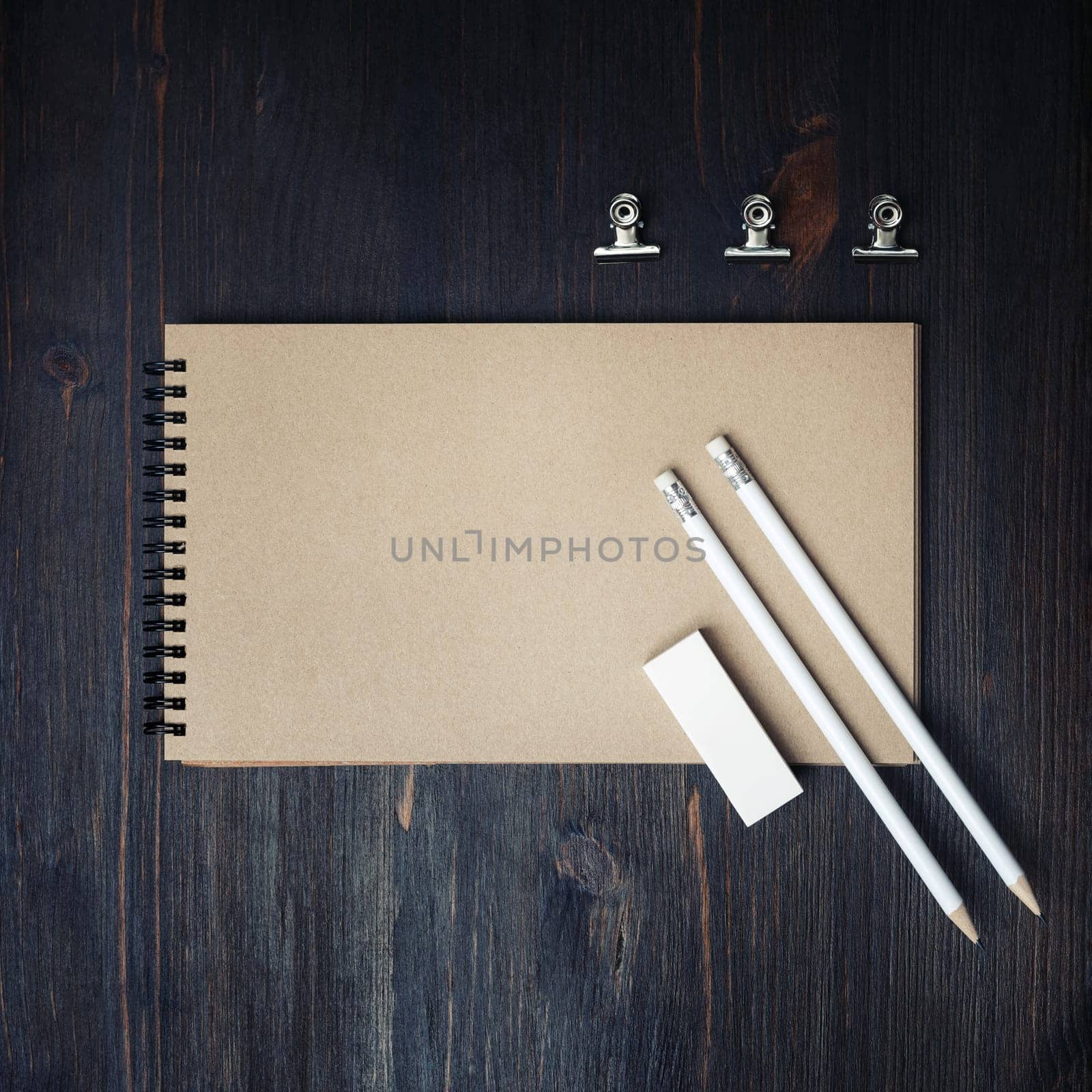 Photo of closed blank kraft sketchbook, pencils and eraser on wood table background. Template for placing your design. Flat lay.