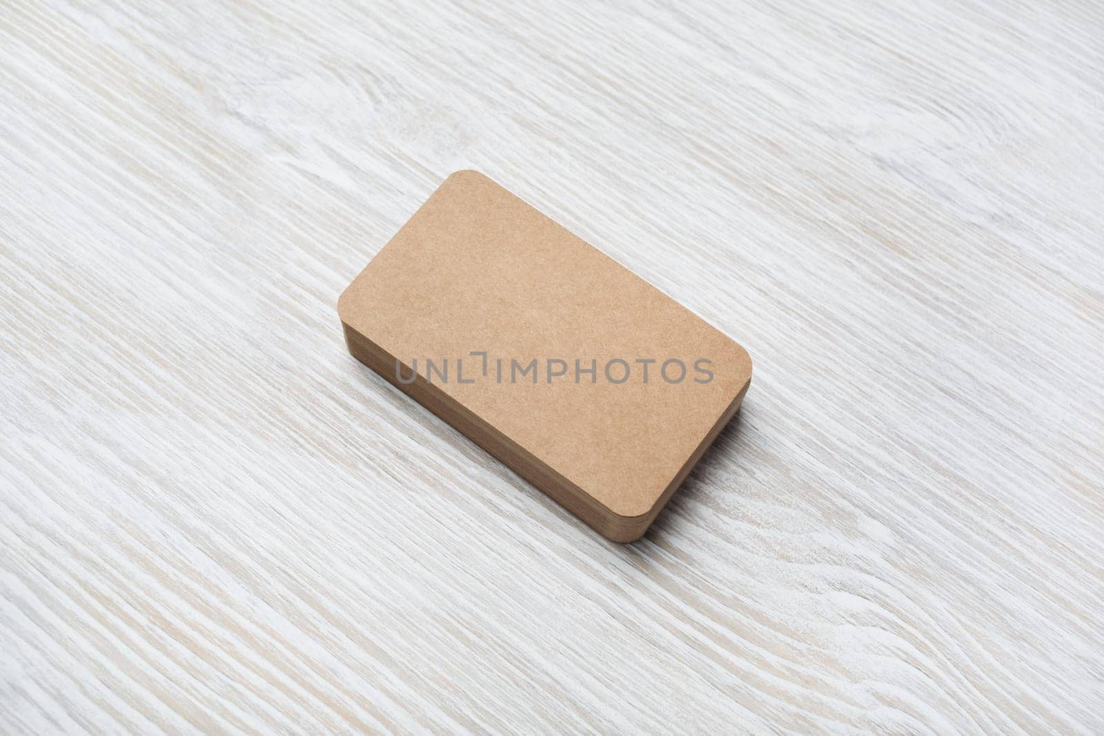 Photo of blank kraft business card on light wood table background. Mock-up for branding identity.