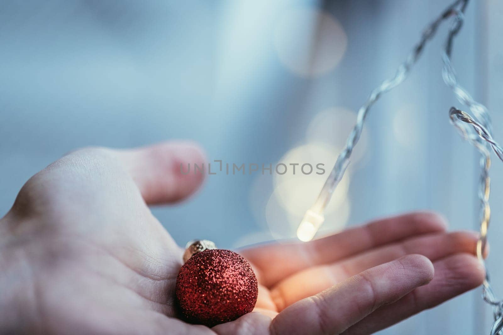 Hand holding a small red christmas bauble, shiny background