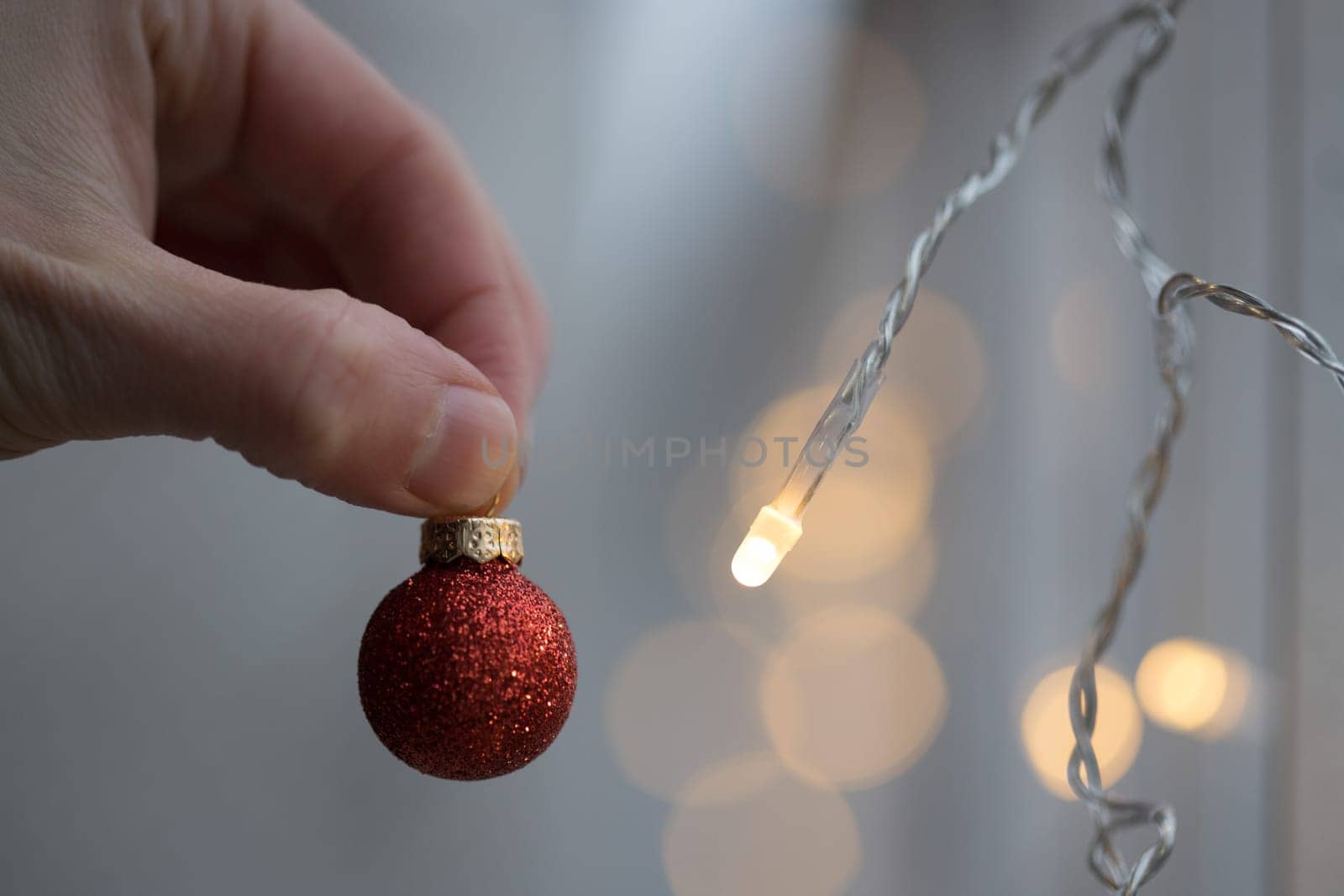 Hand holding a small red christmas bauble, shiny background