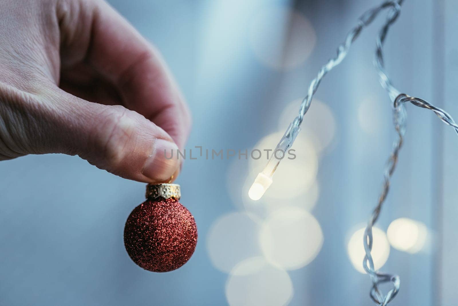 Hand holding a small red christmas bauble, shiny background