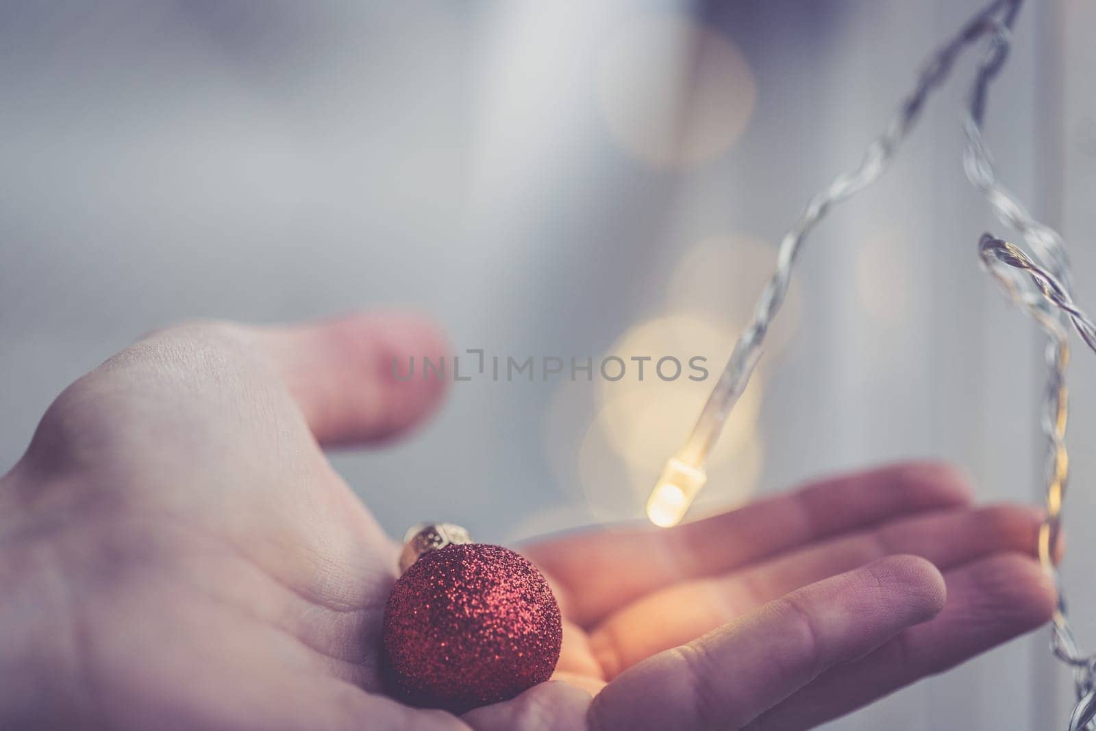 Hand holding a small red christmas bauble, shiny background
