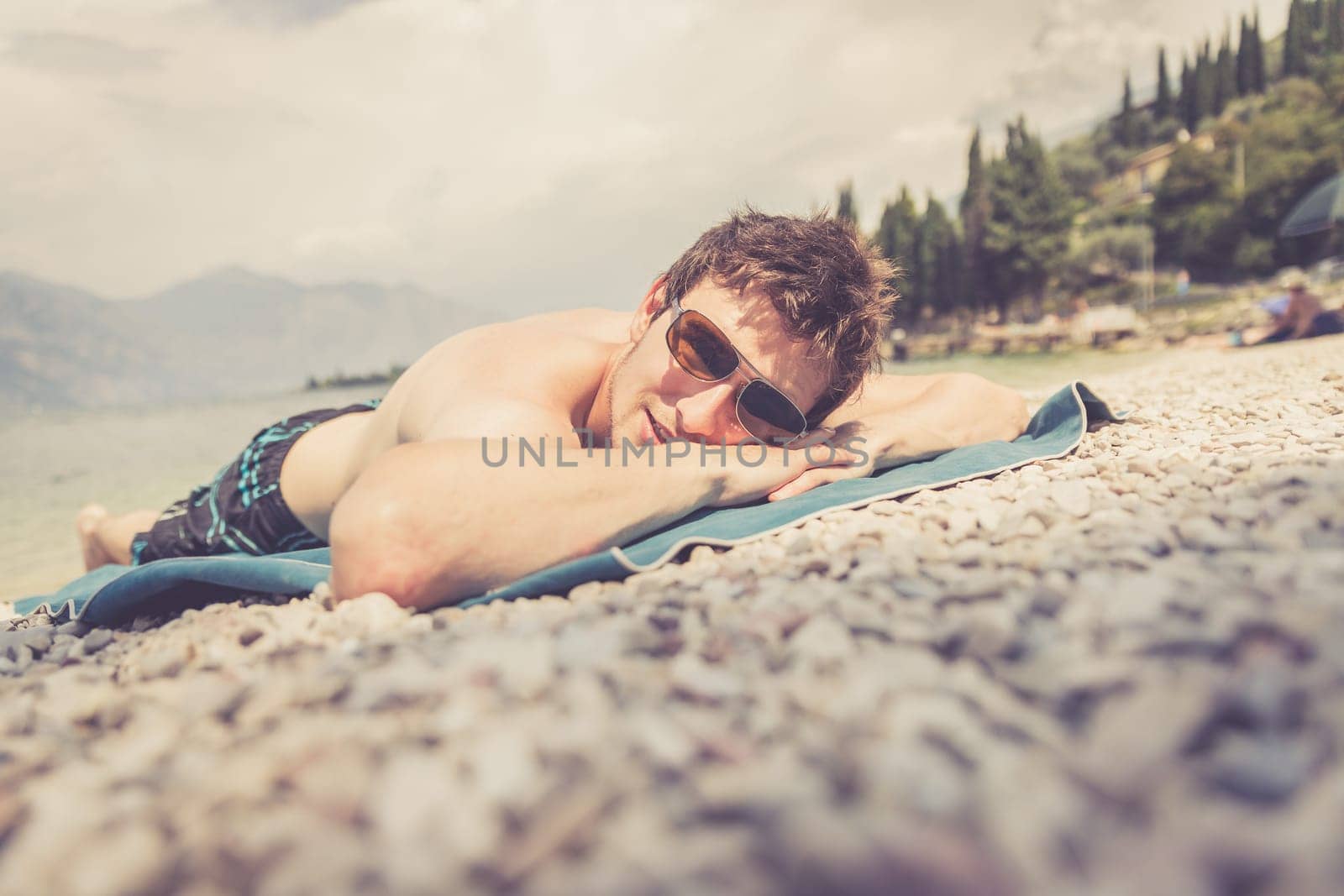 Young handsome man is lying on the beach, sun glasses