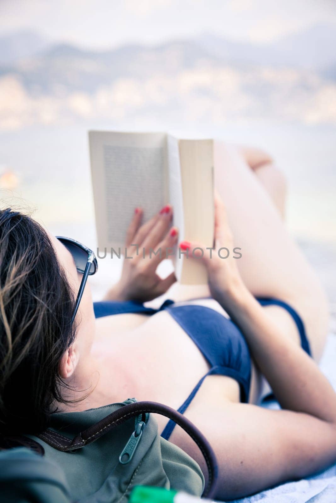 Young beautiful woman in bikini reading a book on the beach