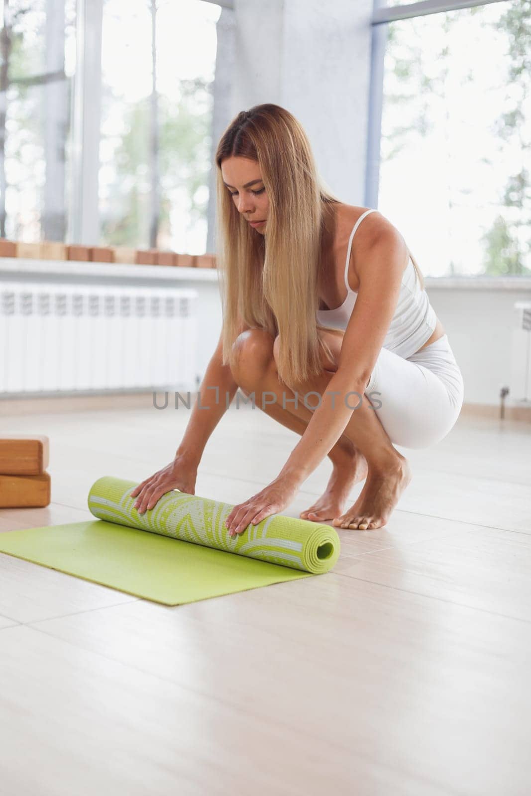 A barefoot woman twists a purple yoga mat and fitness on the parquet floor.