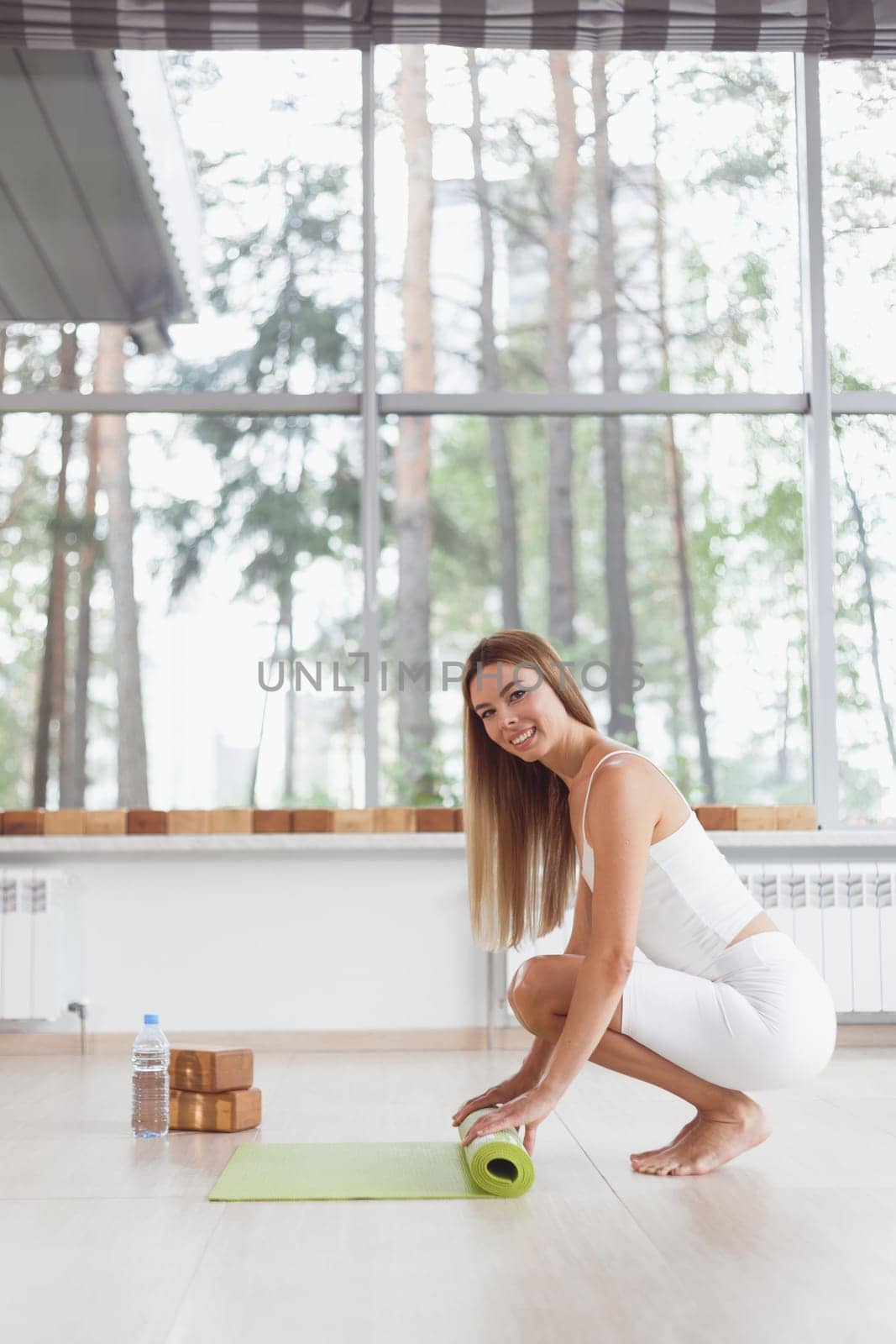 A barefoot woman twists a purple yoga mat and fitness on the parquet floor.
