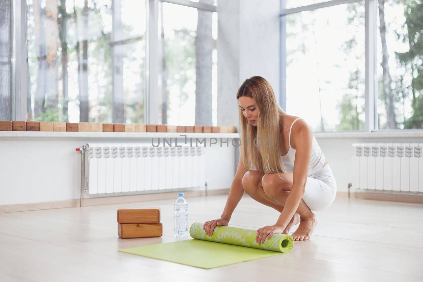 A barefoot woman twists a purple yoga mat and fitness on the parquet floor.