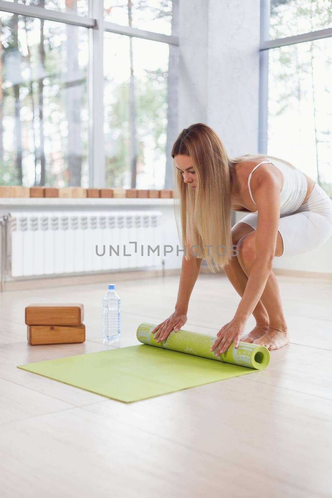 A barefoot woman twists a purple yoga mat and fitness on the parquet floor.