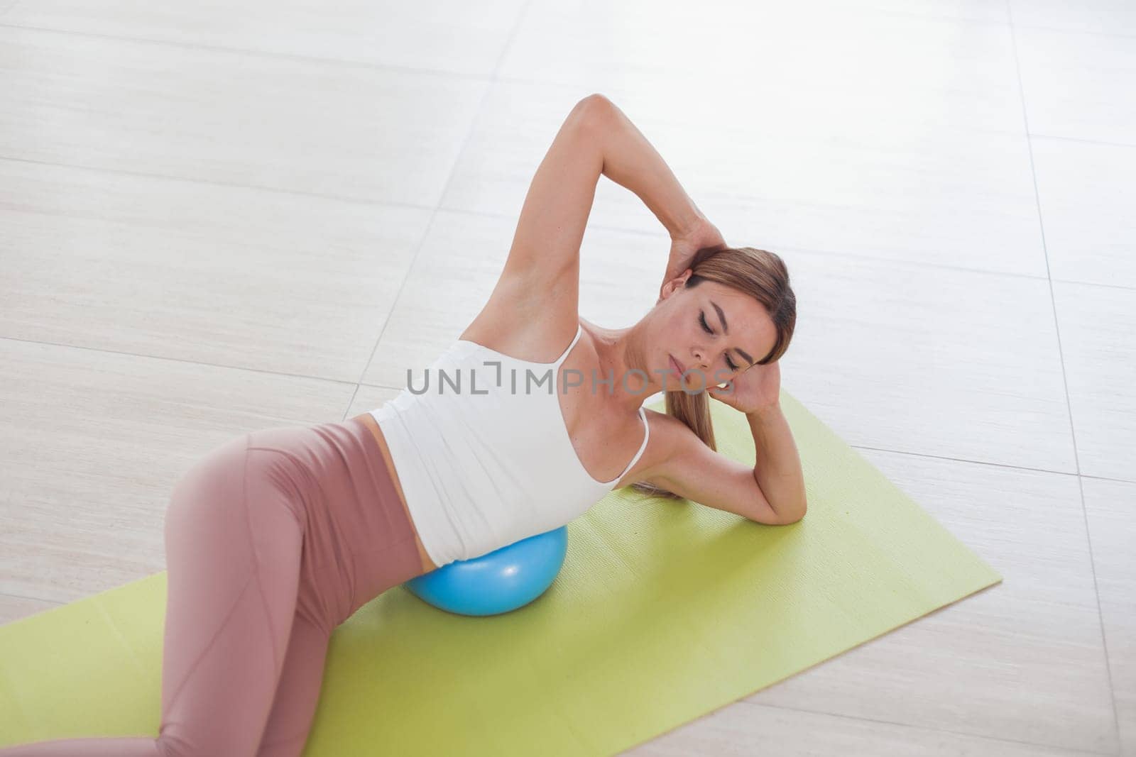 Young woman working out with a ball indoors on green mat.
