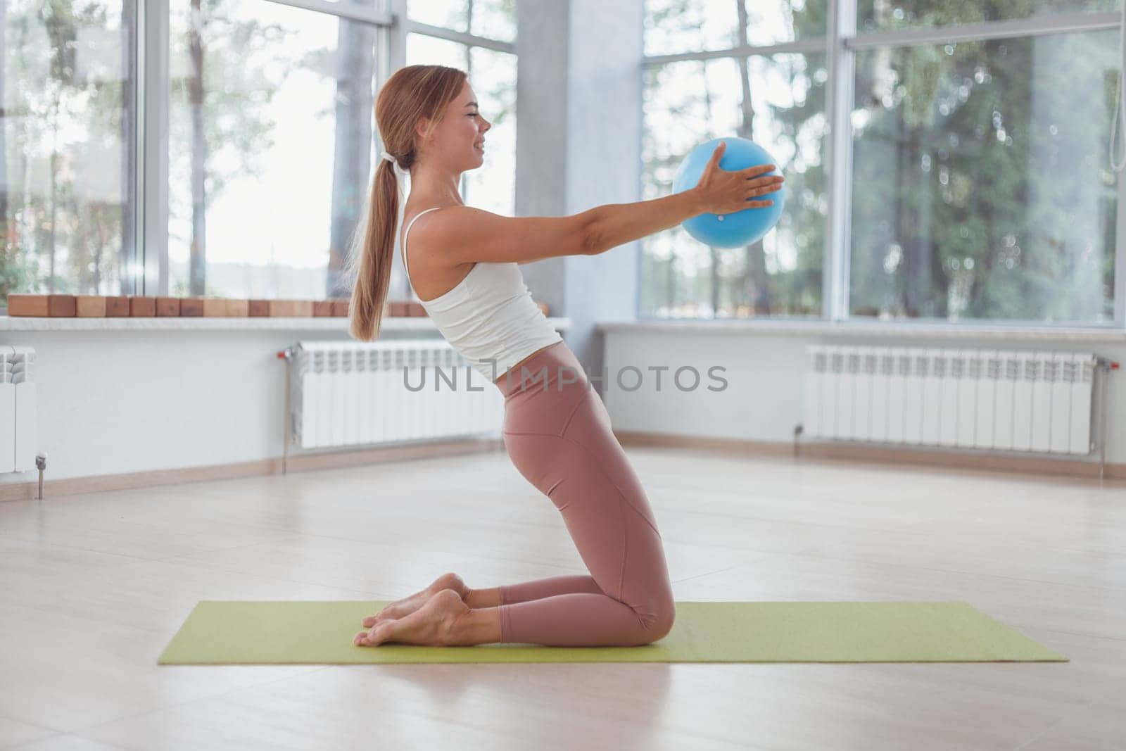 Young woman working out with a ball indoors on green mat.