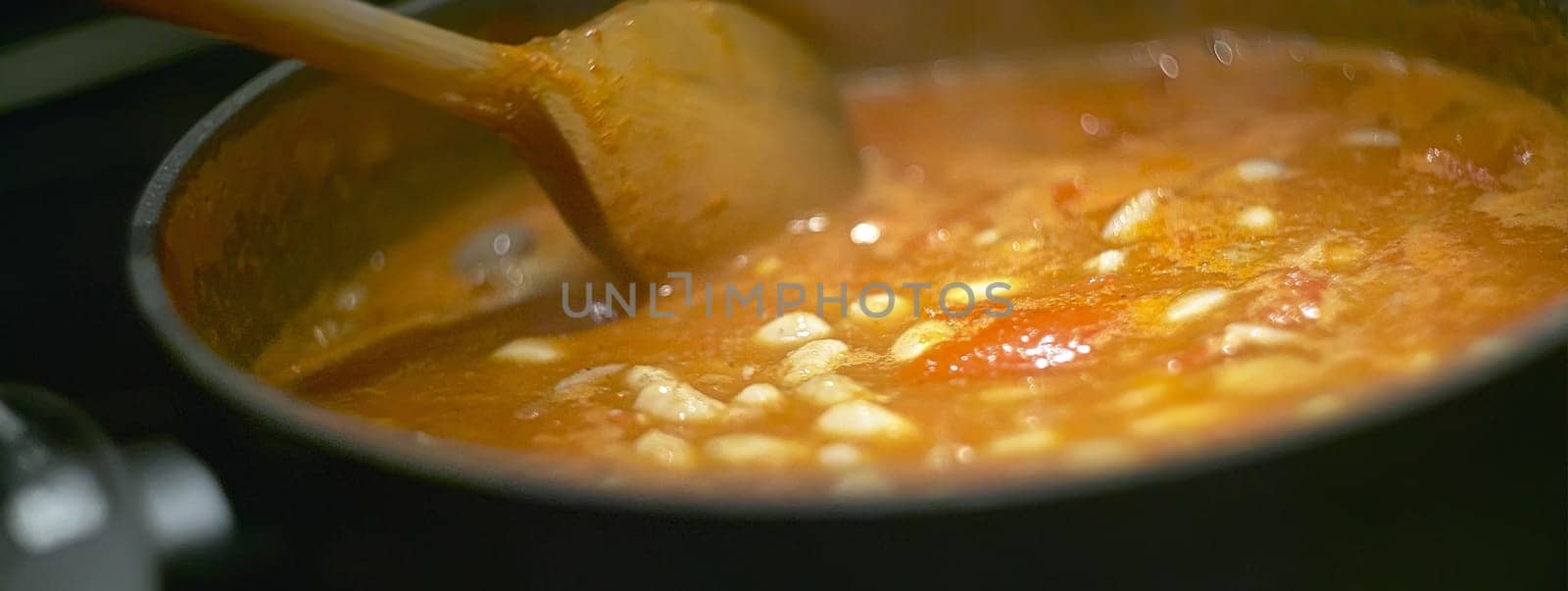 Pot of gravy or soup while cooking on the stove and is stirred to achieve the perfect cooking to be served.