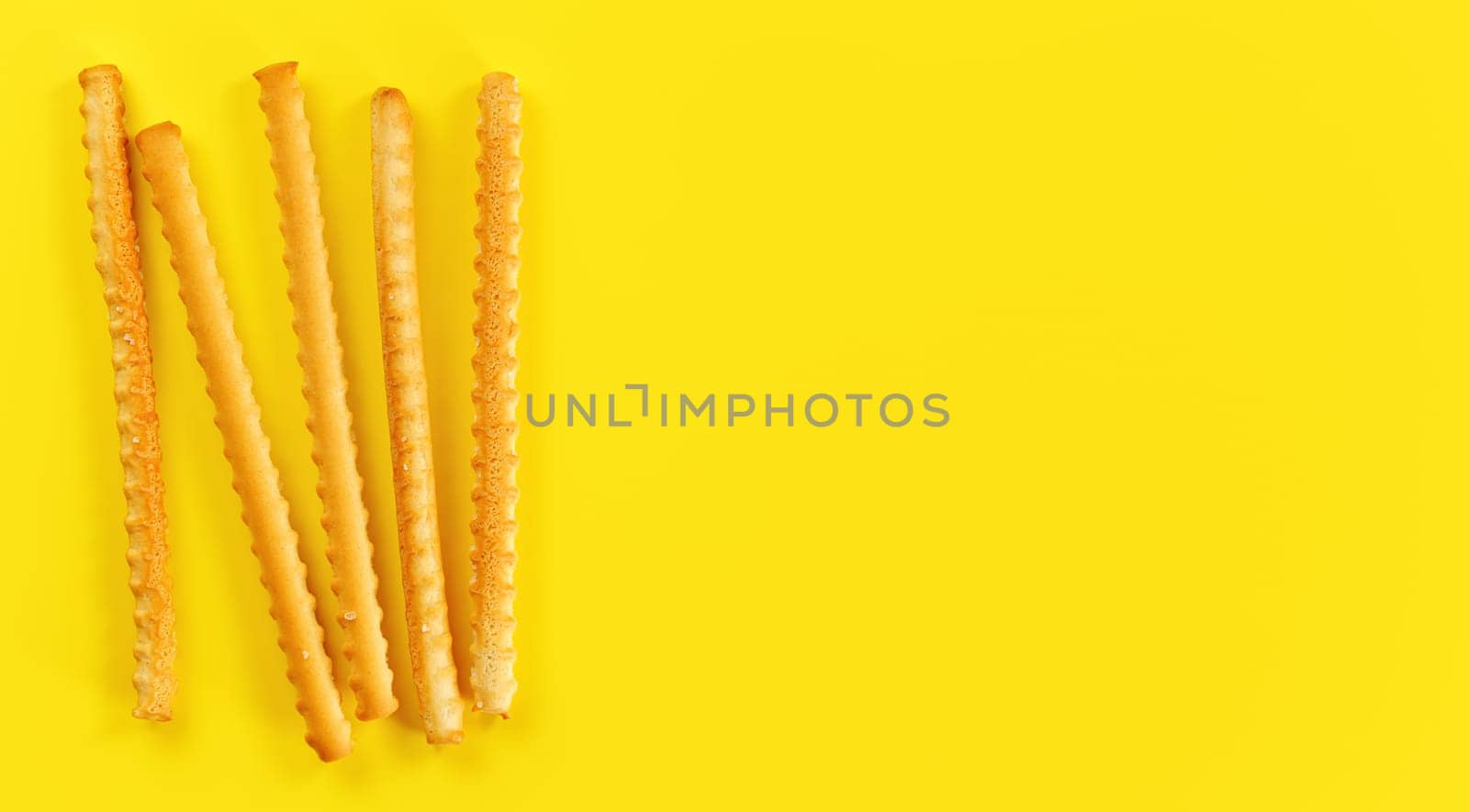Grissini, also known as breadsticks on yellow board, view from above space for text right side.