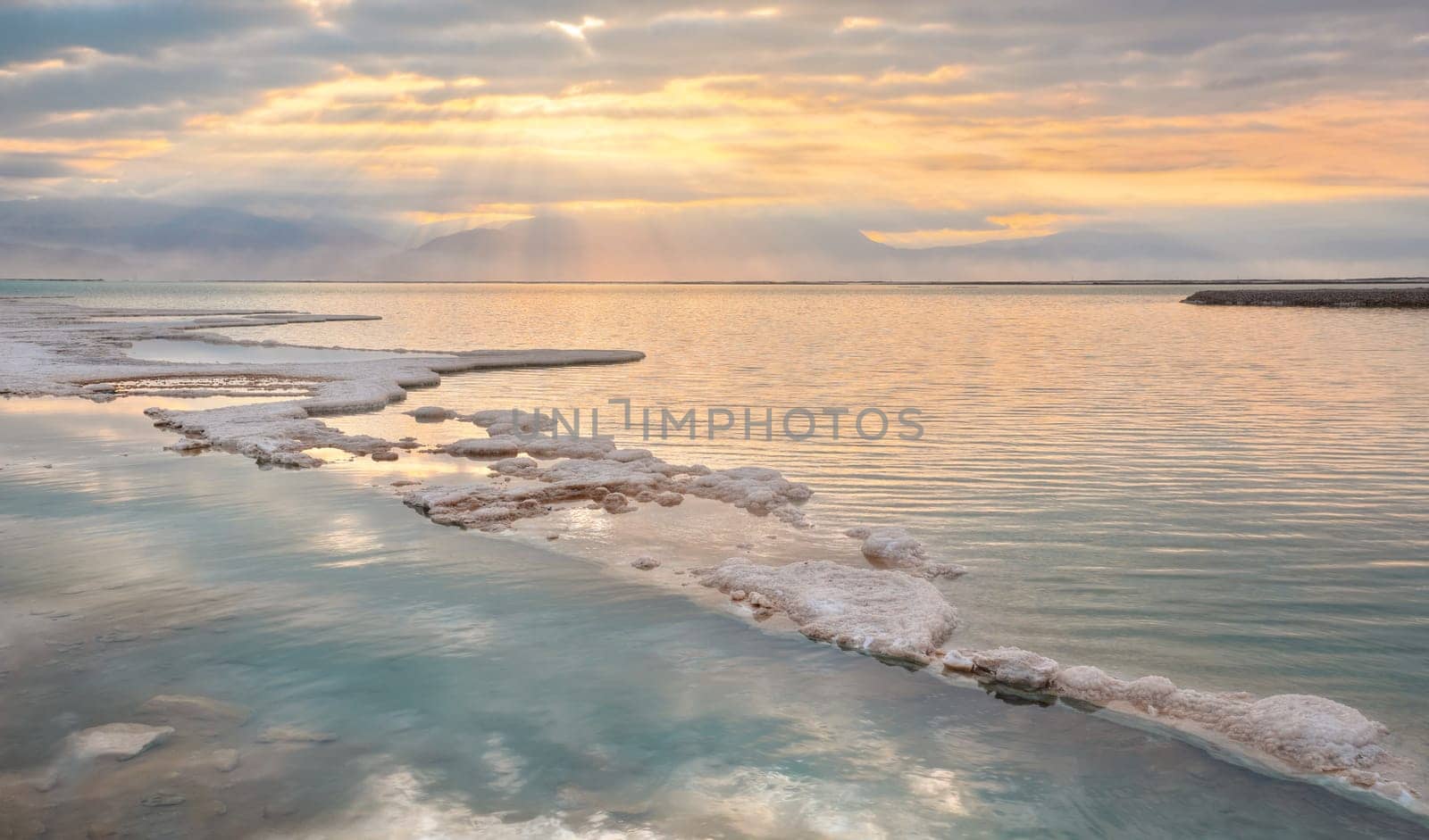 Morning sun shines on salt crystals formations, clear cyan green calm water near, typical landscape at Ein Bokek beach, Israel.