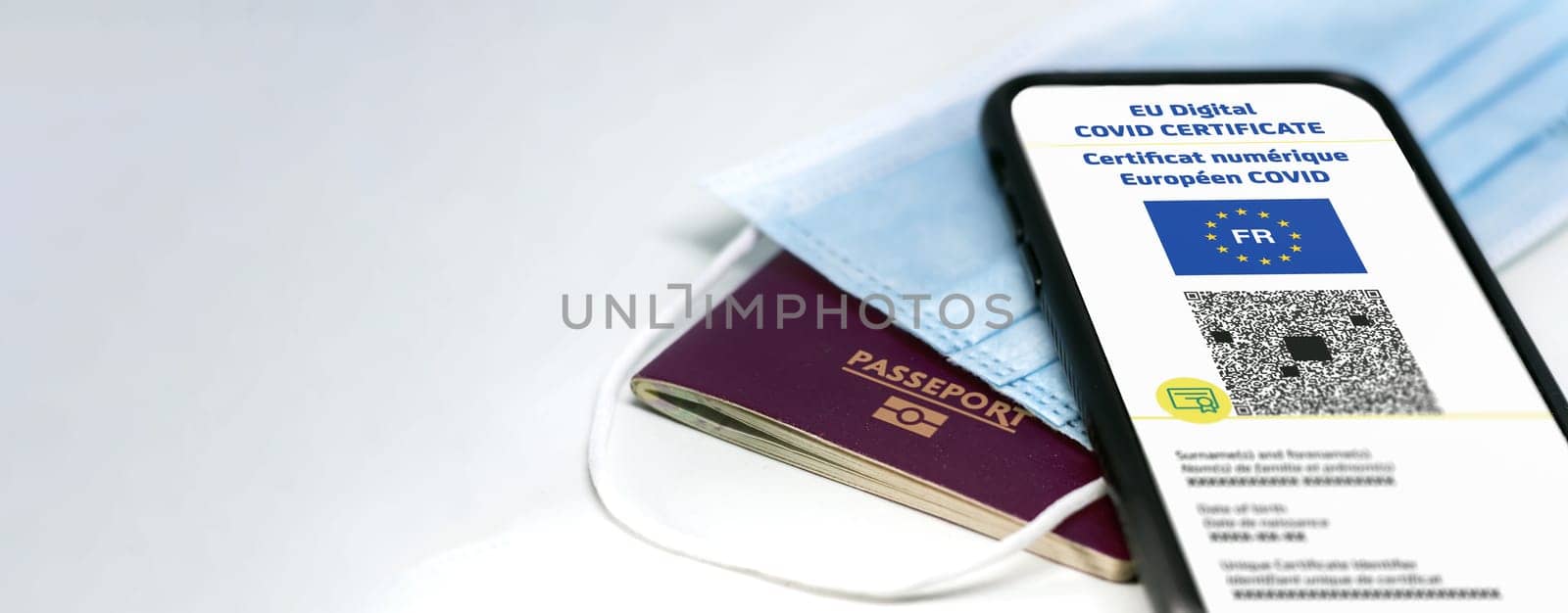 French EU Digital COVID Certificate with the QR code. Translation from french "European COVID digital certificate"". Mobile phone over a surgical mask and a french passport. Health passport. Copy space"