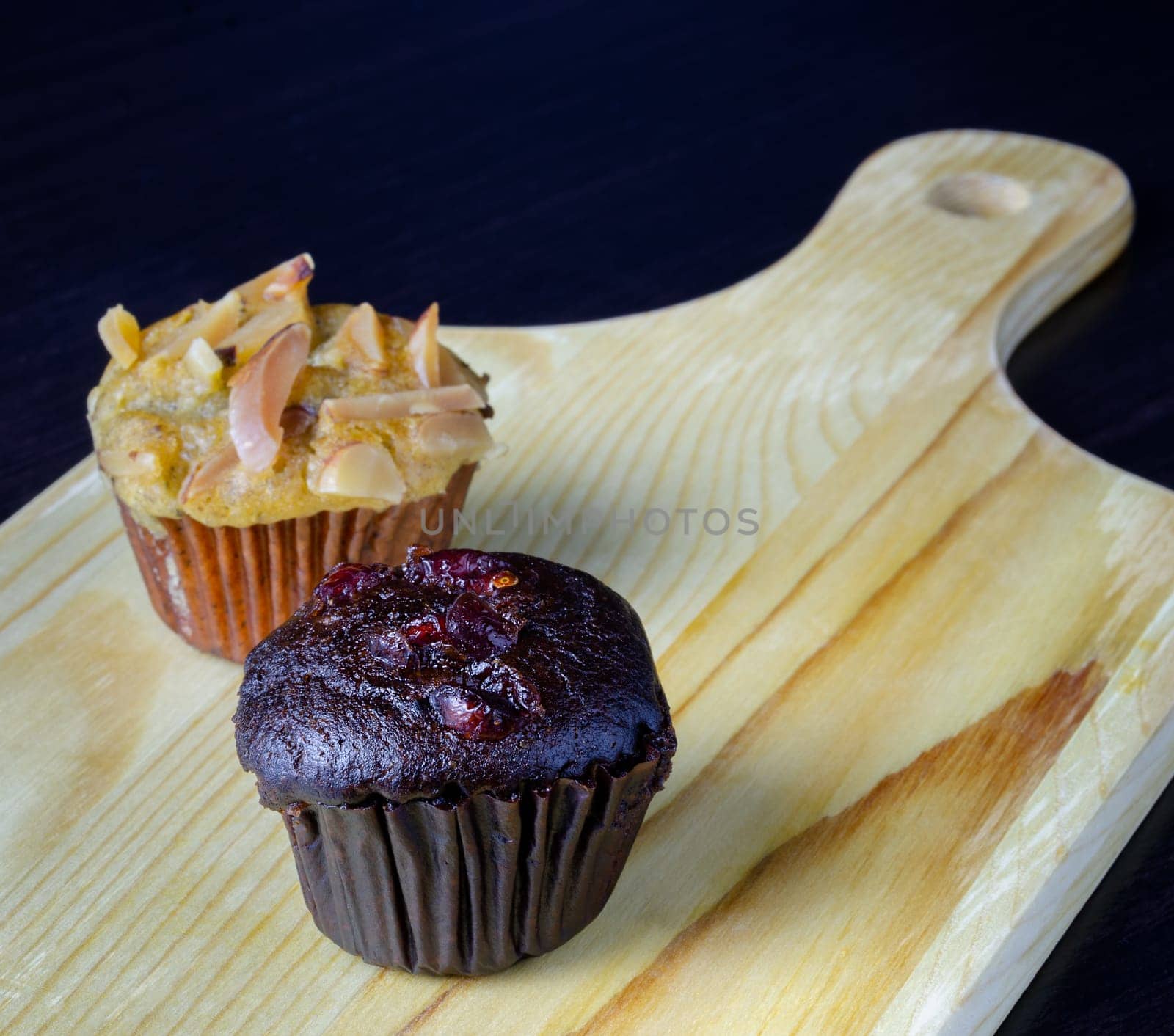 Chocolate cherry muffin and banana cupcake with almond toping on wooden board