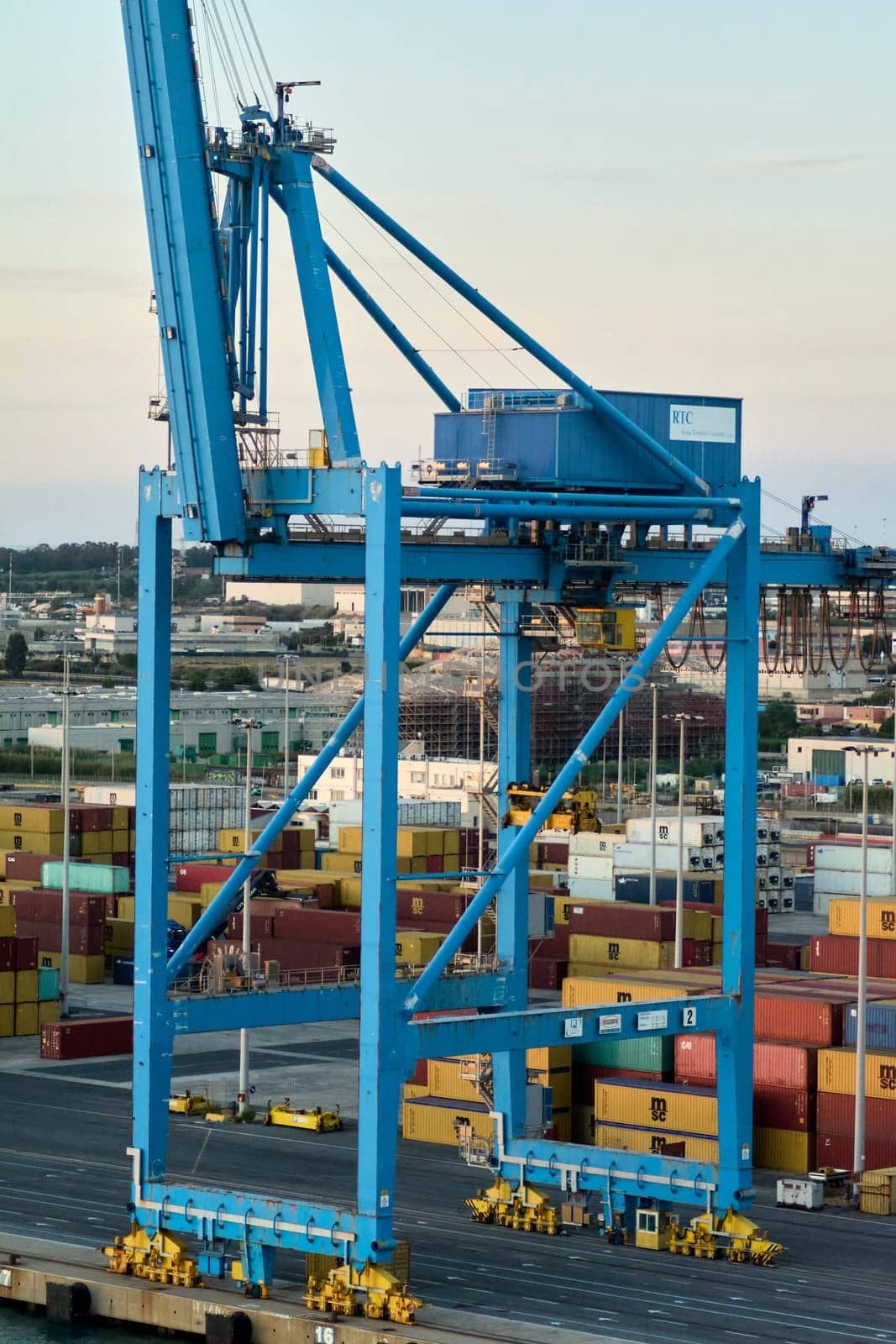 Civitavecchia. Italy - February 17, 2025: Impressive blue crane at Civitavecchia handling containers amidst a bustling shipping environment. Ideal for illustrating industrial and maritime activities.