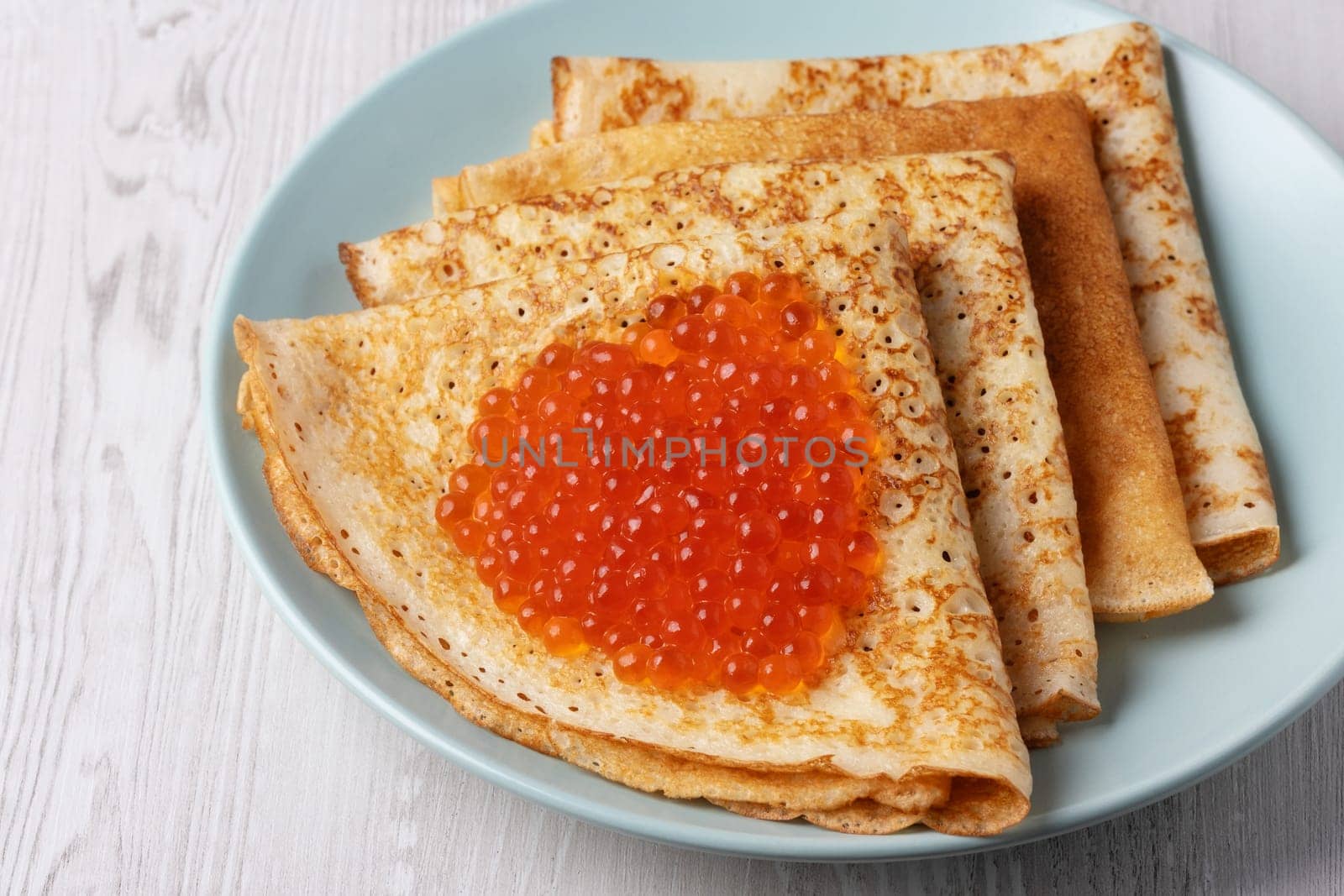 Savory crepes filled with fresh orange fish roe served on a light blue plate at a cozy breakfast table.