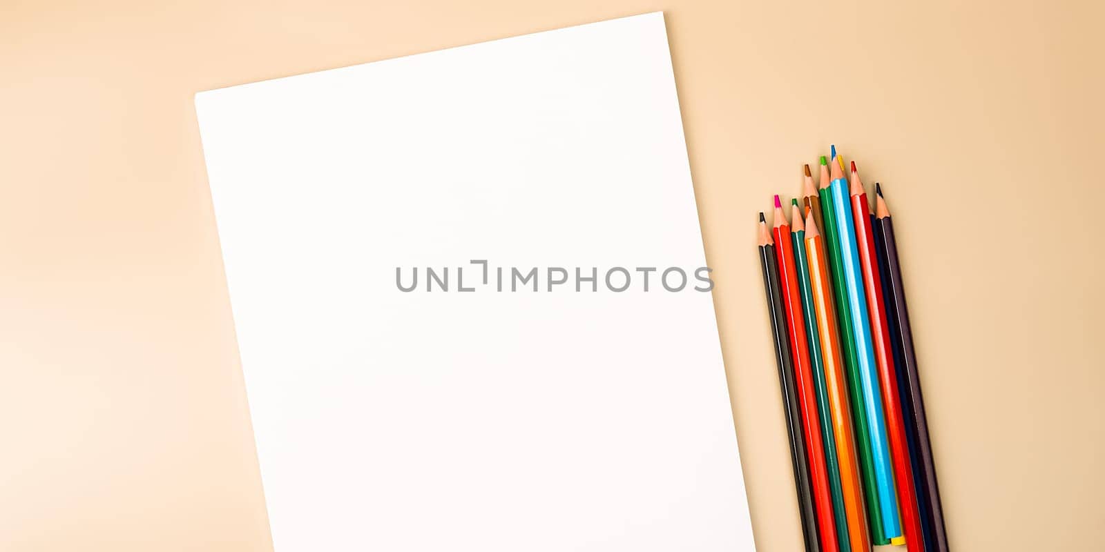 A blank white sheet and colored pencils for drawing on a plain textured background with space for copying and lettering. Layout, mockup free space.