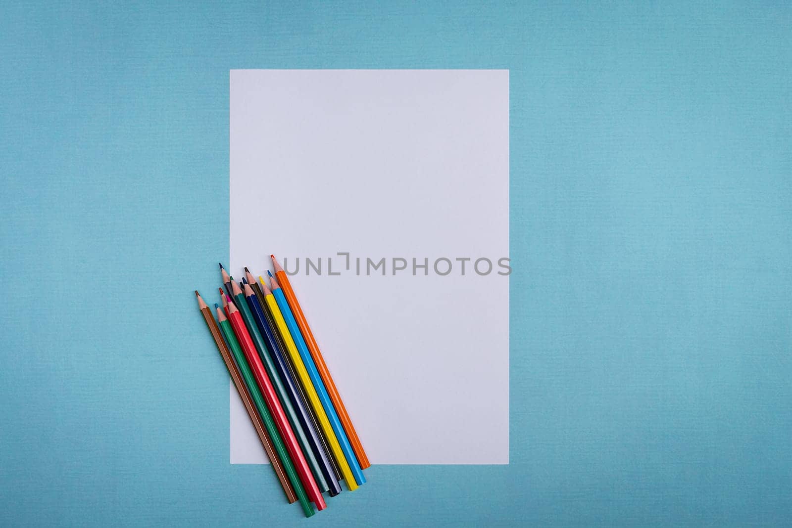 A blank white sheet and colored pencils for drawing on a plain textured background with space for copying and lettering. Layout, mockup free space.