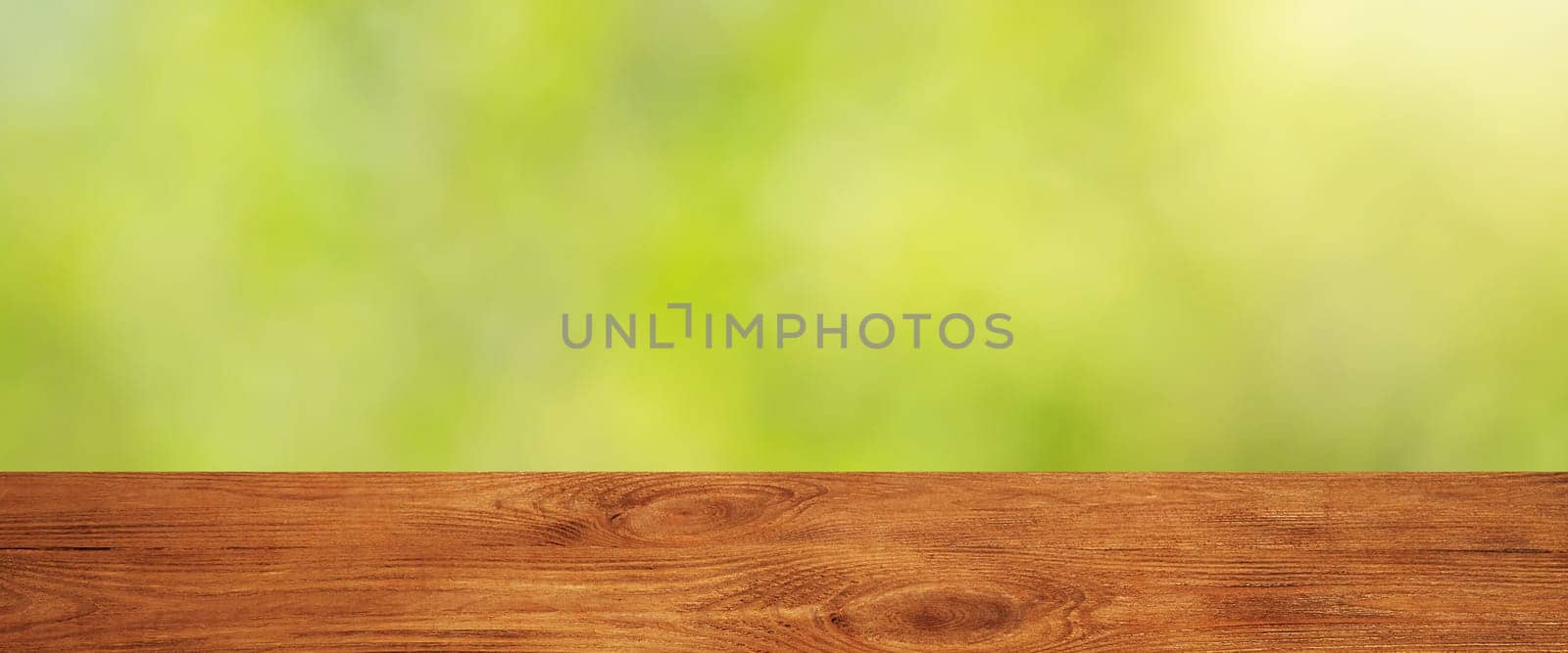 Background with blurred green leaves and empty wooden planks in the foreground. For product demonstrations, free space, layout, mockup, perspective board, background board.