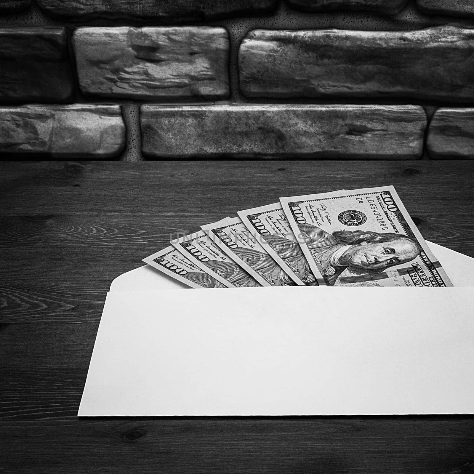Dollars in one-hundred-dollar bills are spread out in an envelope on a table near the brick wall. Dollars fanned out. US dollars. On the envelope there is a place for an inscription, a logo. Black and white style. Layout, template, mockup.