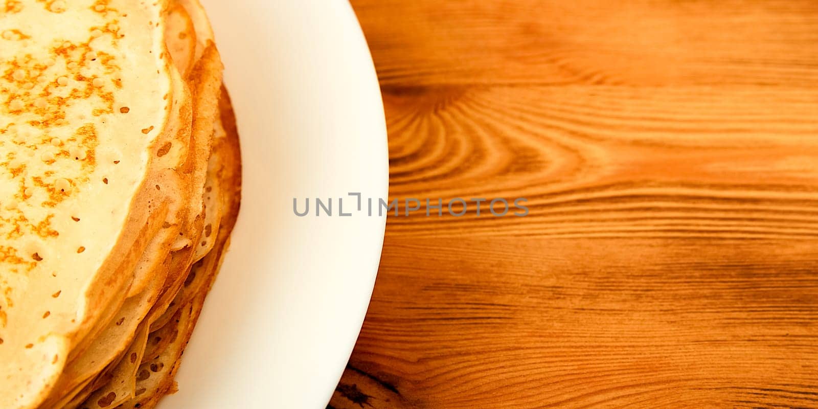 Pancakes on a plate on a wooden table. A large stack of fresh pancakes. Delicious healthy fresh pancakes. Place for advertising, logo, lettering, layout, mockup.