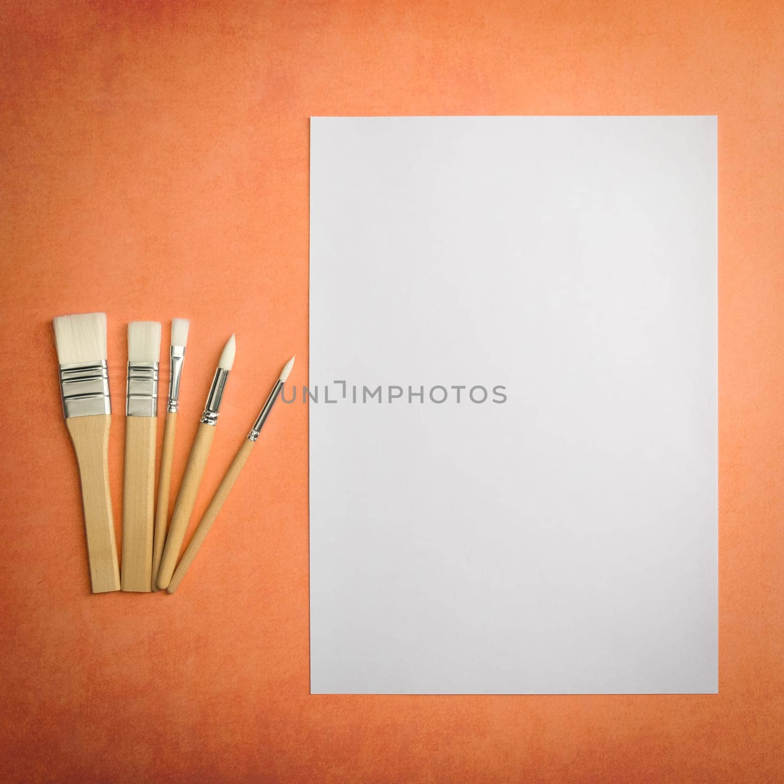 A clean white sheet and brushes on a textured background with space to copy. Layout, mockup space for text and drawing.